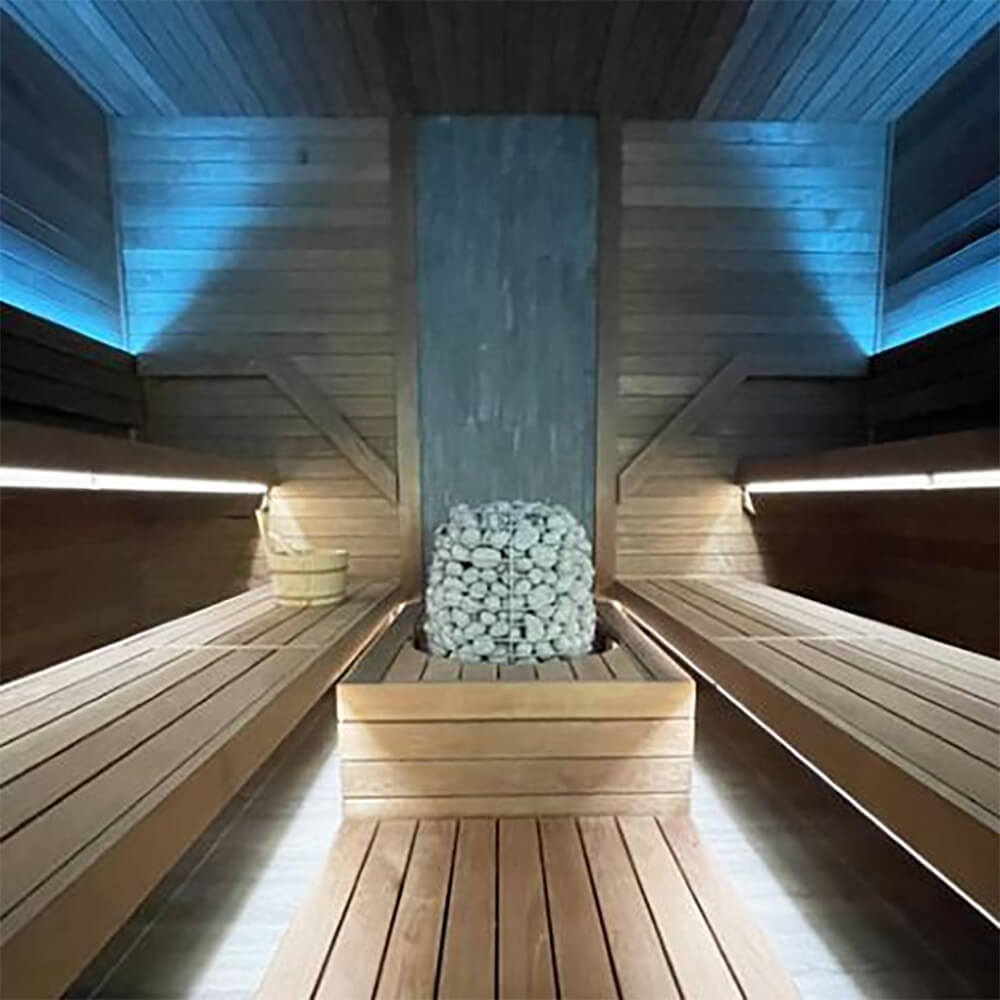 Huum Hive Premium 18kW floor-mounted sauna heater by SAKSBY WHOLESALE with UKU control, extension box, and sauna stones inside a sauna room.