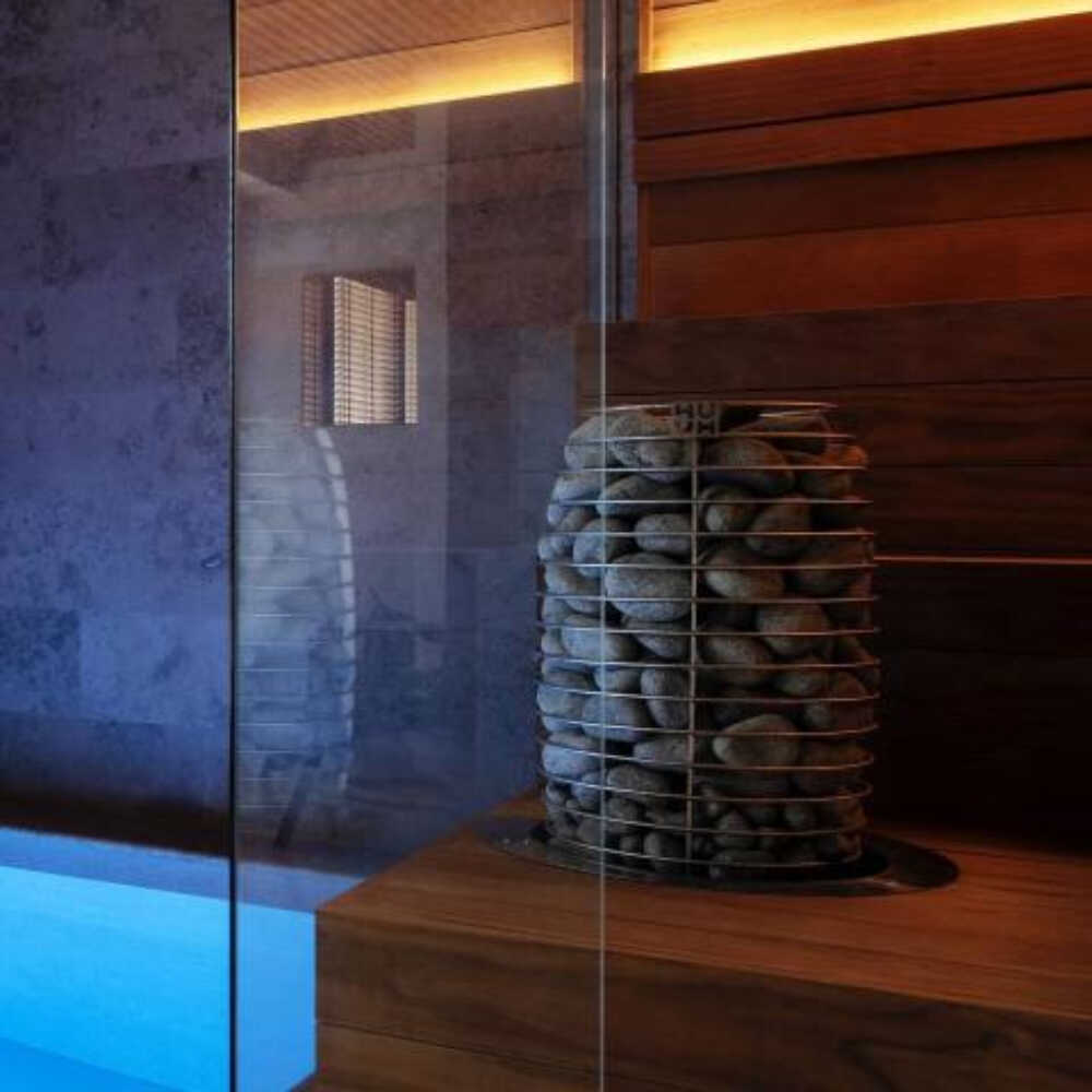 Huum Hive Mini steel sauna heater with digital controller and sauna stones, floor-mounted, shown from left side view.