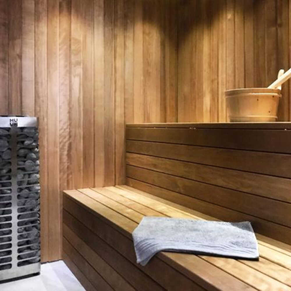 Stainless steel wall-mounted sauna heater from Huum Steel Series with UKU control and sauna stones, suitable for small sauna rooms.