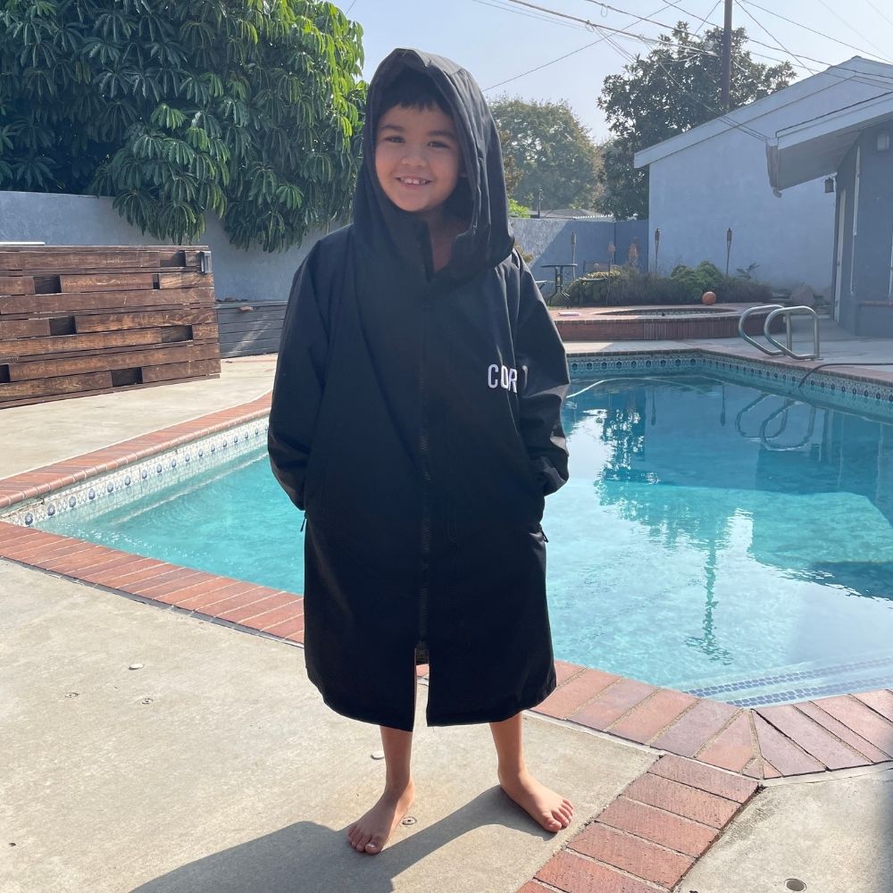 Kids waterproof swim parka by COR Surf in black, lightweight and waterproof, perfect for outdoor swimming and beach days.