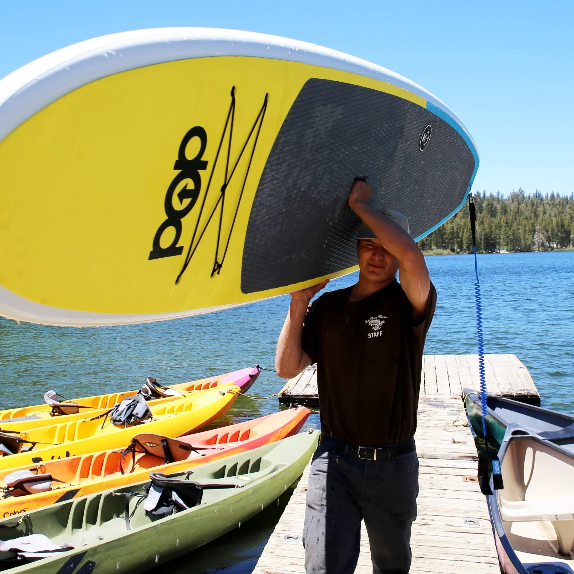 Yellow and blue 10'6" Amigo wood paddle board by Backcountry Sportsman, shown on calm water with paddle.
