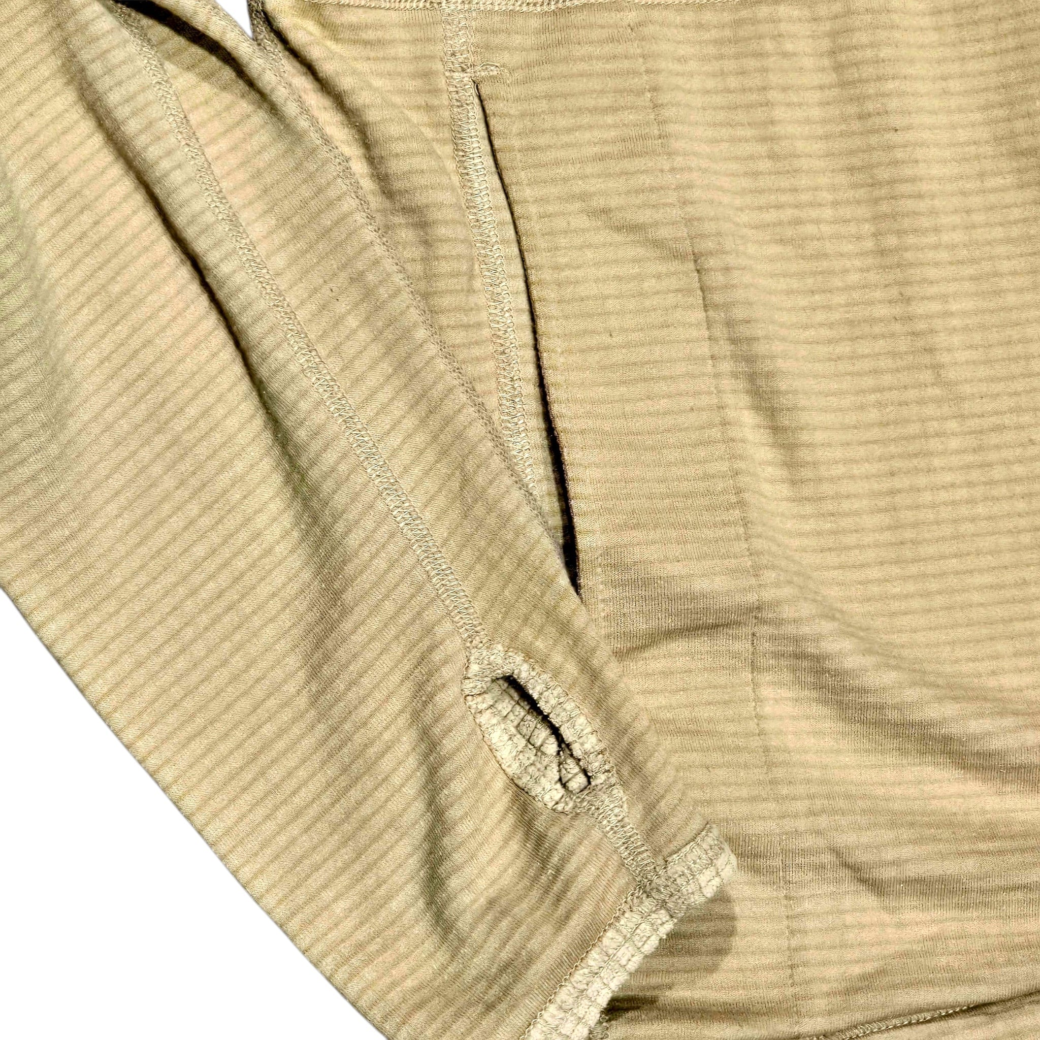 Close-up of a ribbed knit garment in a light beige or oatmeal color, showing the texture and stitching details against a white background.