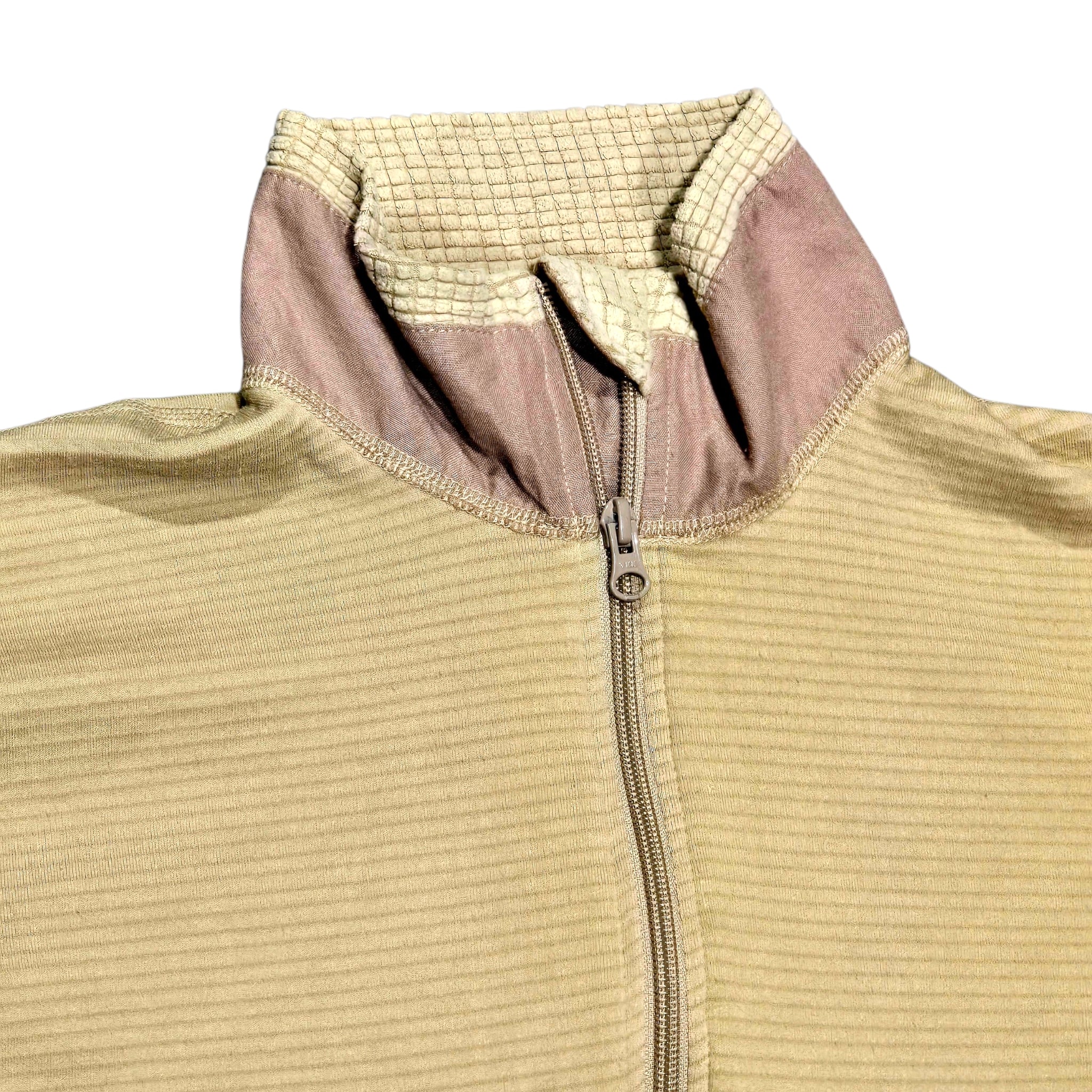 Close-up of a ribbed knit zip-up jacket with a high collar, featuring a beige body and a contrasting dusty pink collar lining.