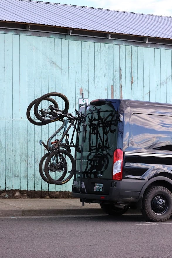 Lolo Racks Rad Lad rear ladder bike rack kit installed on a Ford Transit van, securely holding bicycles on the vehicle's rear ladder.