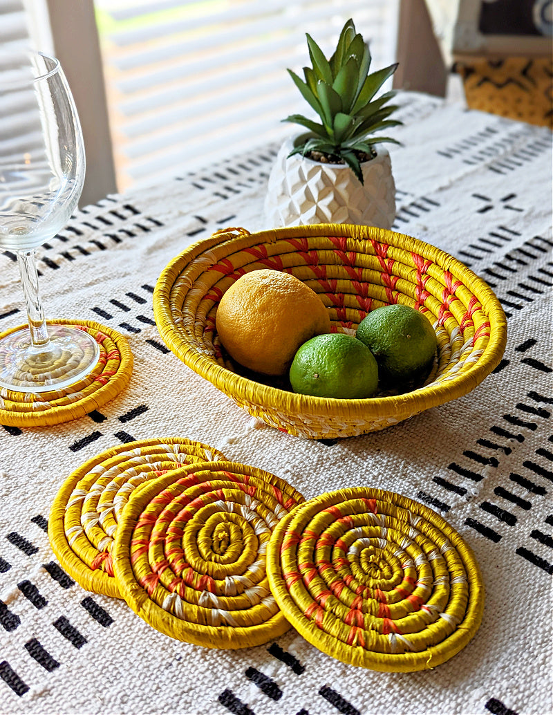 Set of four handmade woven drink coasters with small yellow baskets by Reflektion Design, featuring multiple vibrant colors.