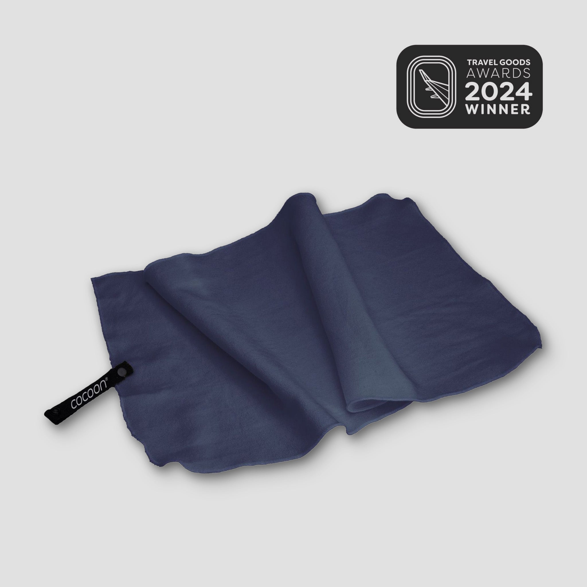 COCOON Hyperlight Travel Towel displayed on a sandy beach, showcasing its lightweight and compact design.