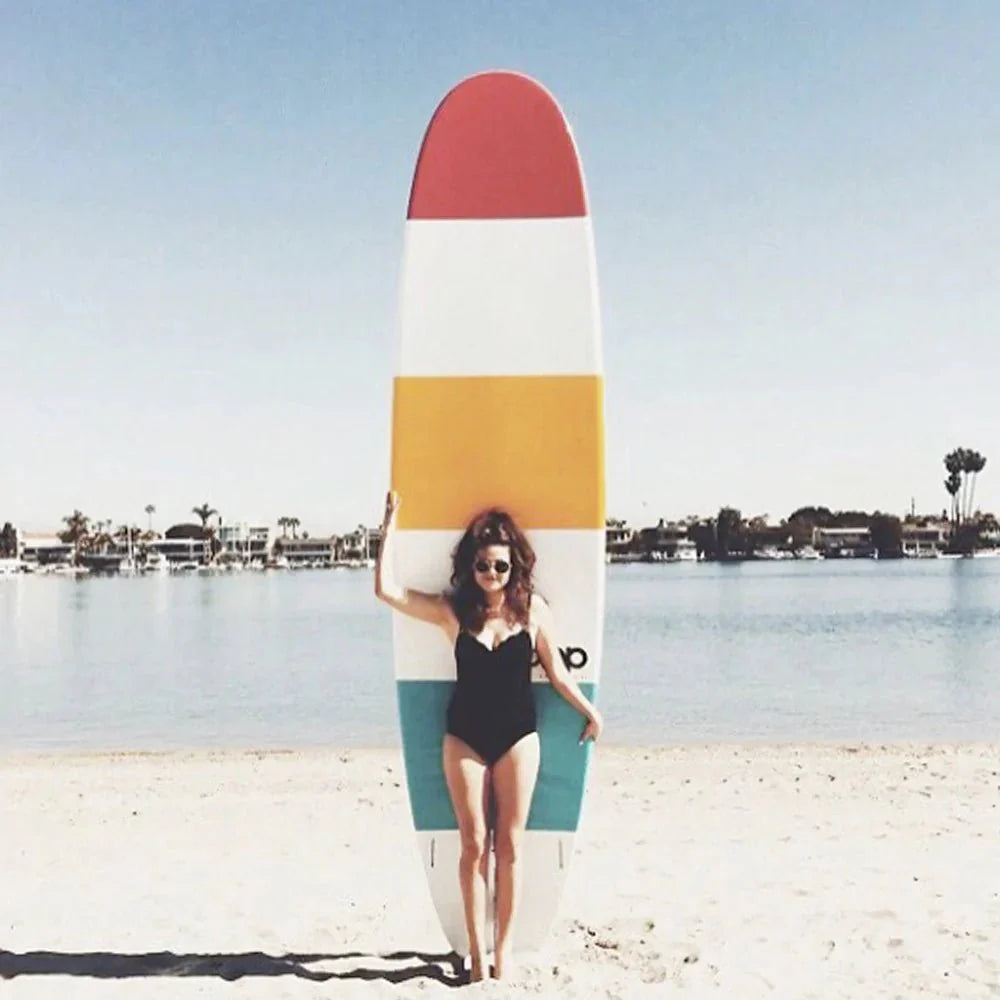 Backcountry Sportsman 11'6 Throwback retro-style surfboard with colorful design, shown on rack with a sandy beach background.