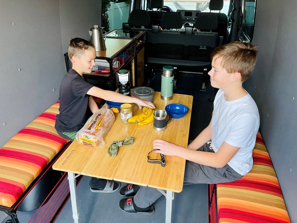 Van wheel well bench storage in a camper van conversion kit by TNTvans, showing a built-in dinette with storage compartments.