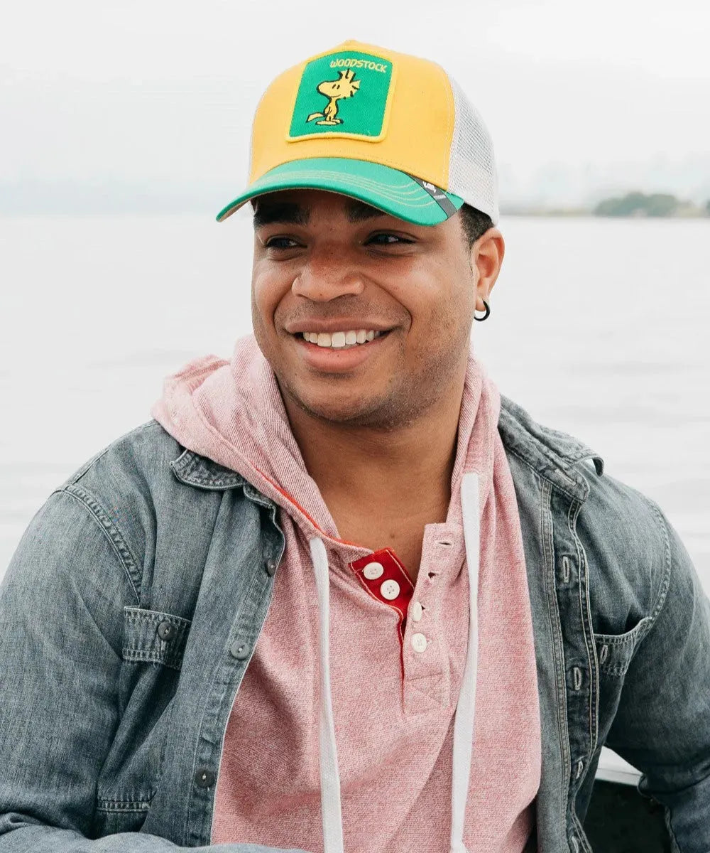 Peter Grimm Peanuts Woodstock yellow trucker cap with cartoon Woodstock design, breathable mesh back, and adjustable snap closure.