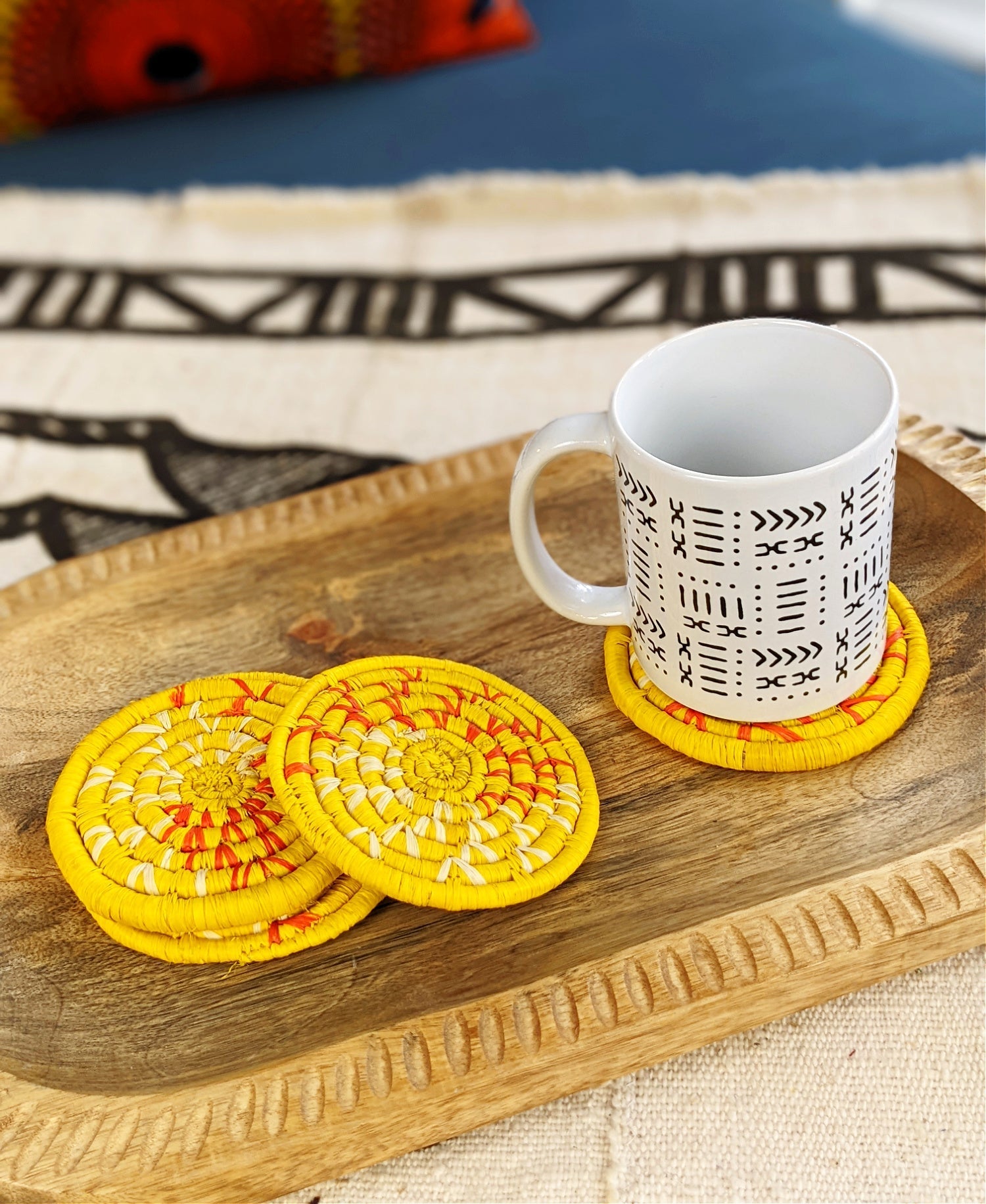 Set of four handmade woven drink coasters in vibrant yellow, featuring colorful patterns from Reflektion Design.